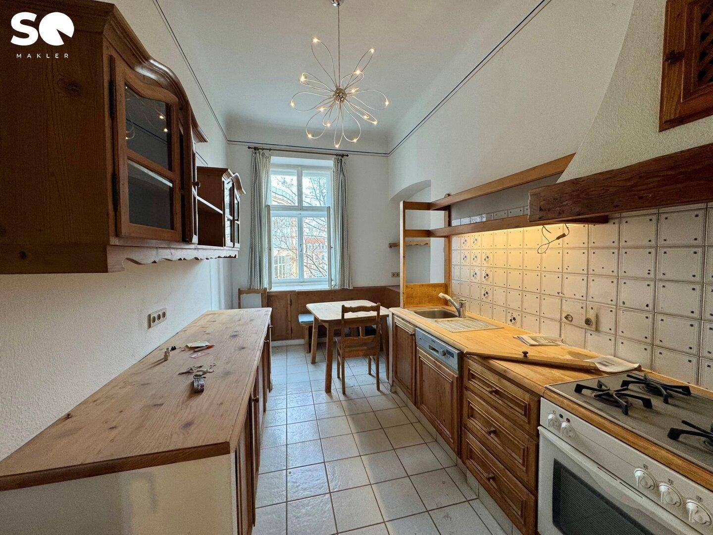 Traditionelle Küche mit Holzelementen, Fliesenboden und Essbereich am Fenster.