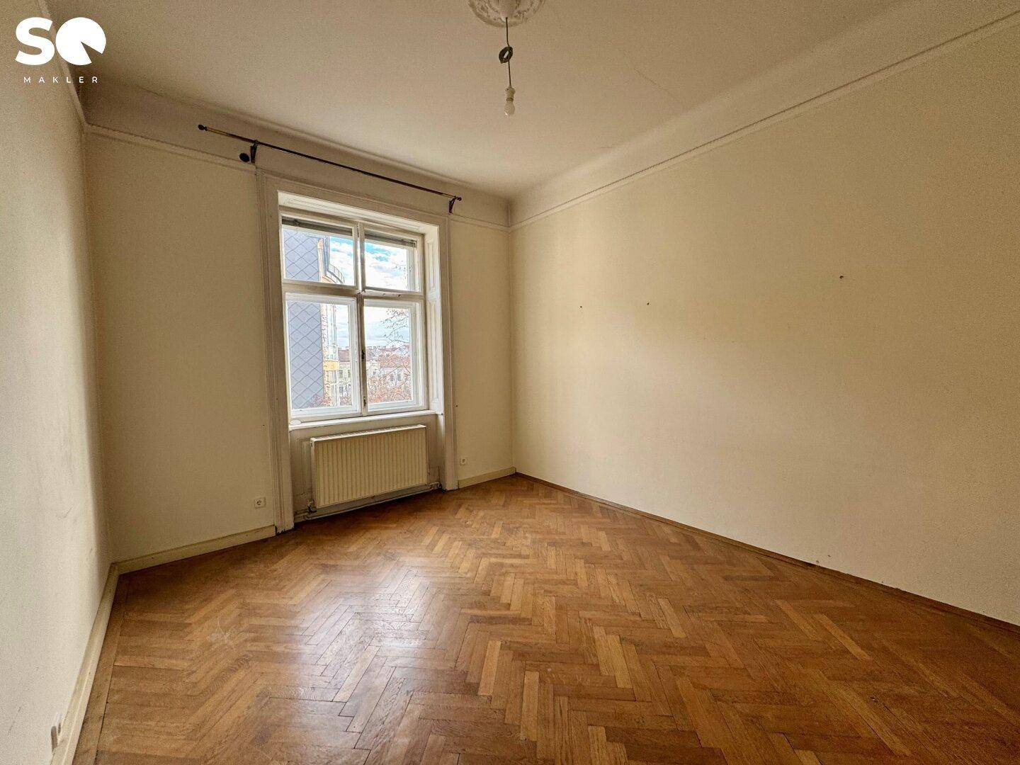 Schlafzimmer mit Fischgrätparkett, hohen Decken und großem Fenster.
