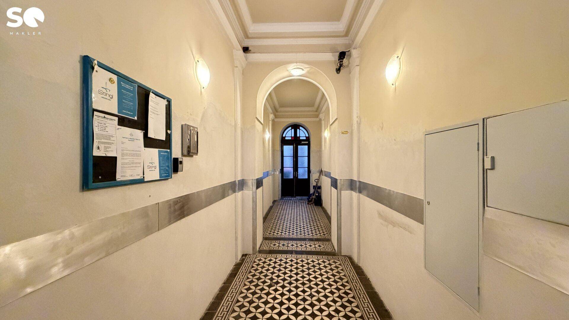 Historischer Eingangsbereich mit gemusterten Fliesen, hohen Decken und klassischer Architektur.