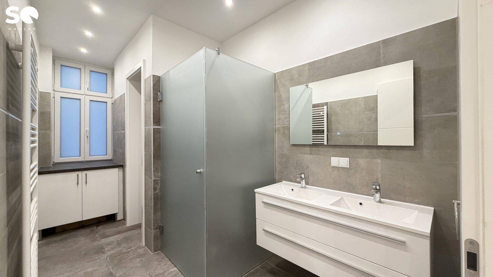 Modernes Badezimmer mit Doppelwaschbecken, großer Dusche und Fenster für natürliche Belüftung.