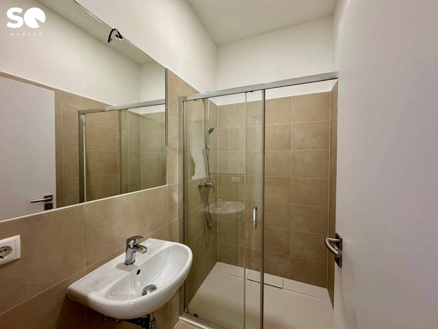 Modernes Badezimmer mit beigefarbenen Fliesen, Duschkabine und Einzelwaschbecken.