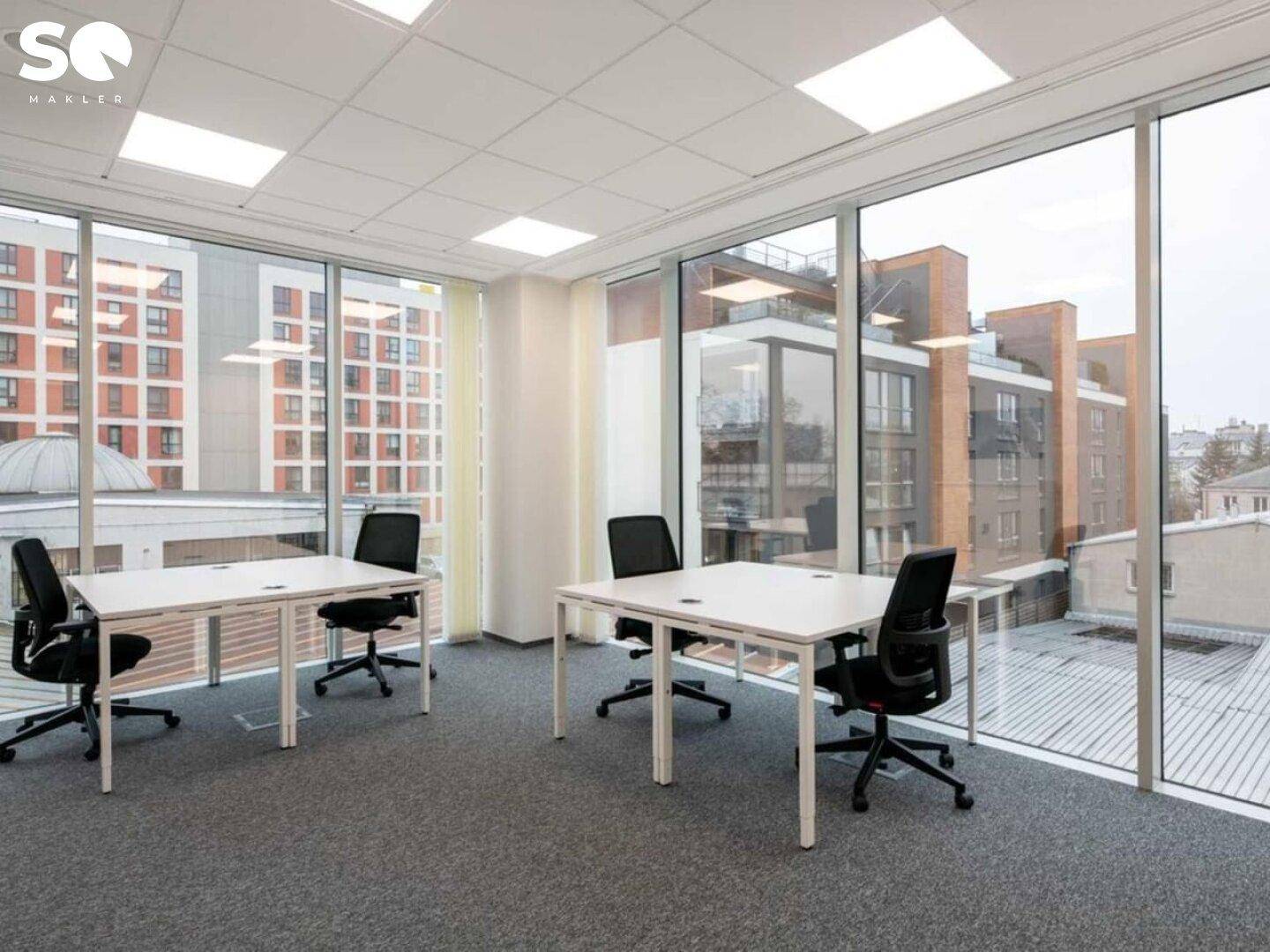 Büro mit großen Fenstern, die einen weiten Blick auf die Stadt und umliegende Gebäude bieten.