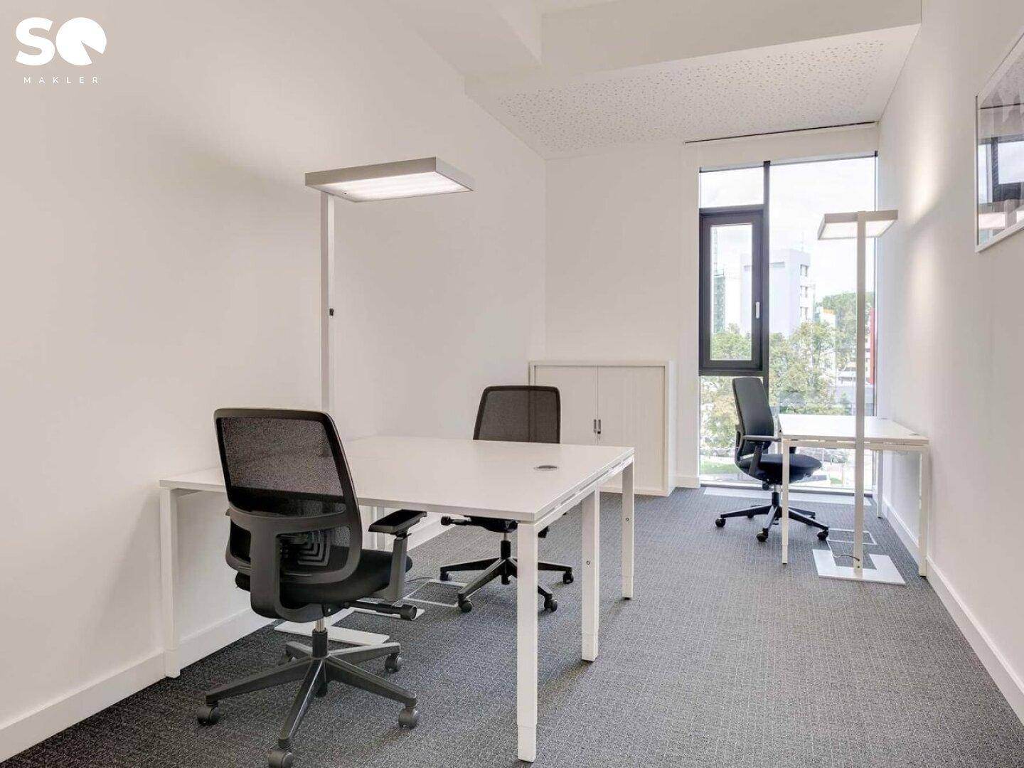 Kleines, helles Büro mit zwei Arbeitsplätzen, großen Fenstern und weiß gestrichenen Wänden.