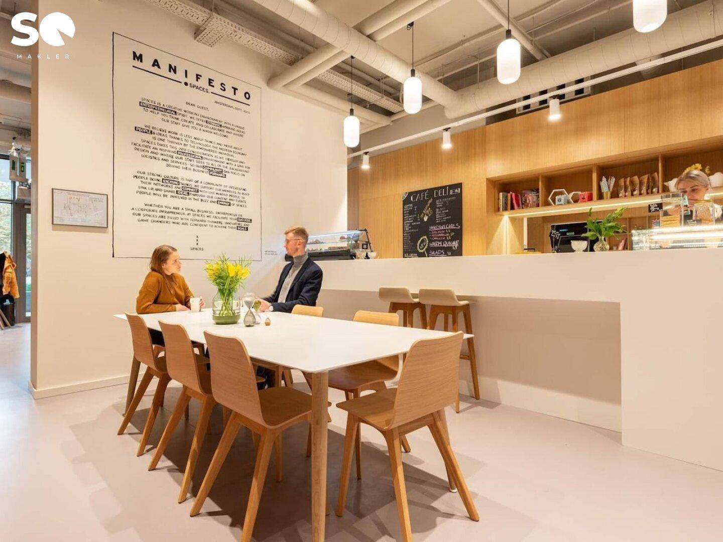 Bürocafé oder Pausenbereich mit Theke, Tischen und Stühlen, wo Menschen sitzen.