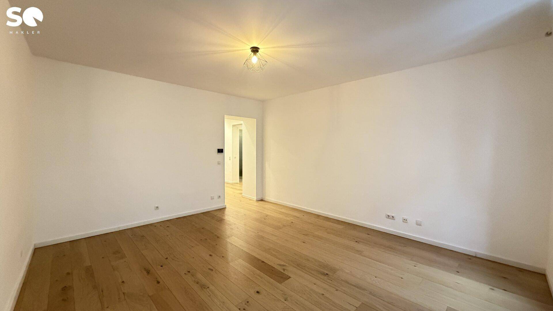 Helles Wohnzimmer mit Parkettboden und Zugang zu einem weiteren Raum, modern und gepflegt.