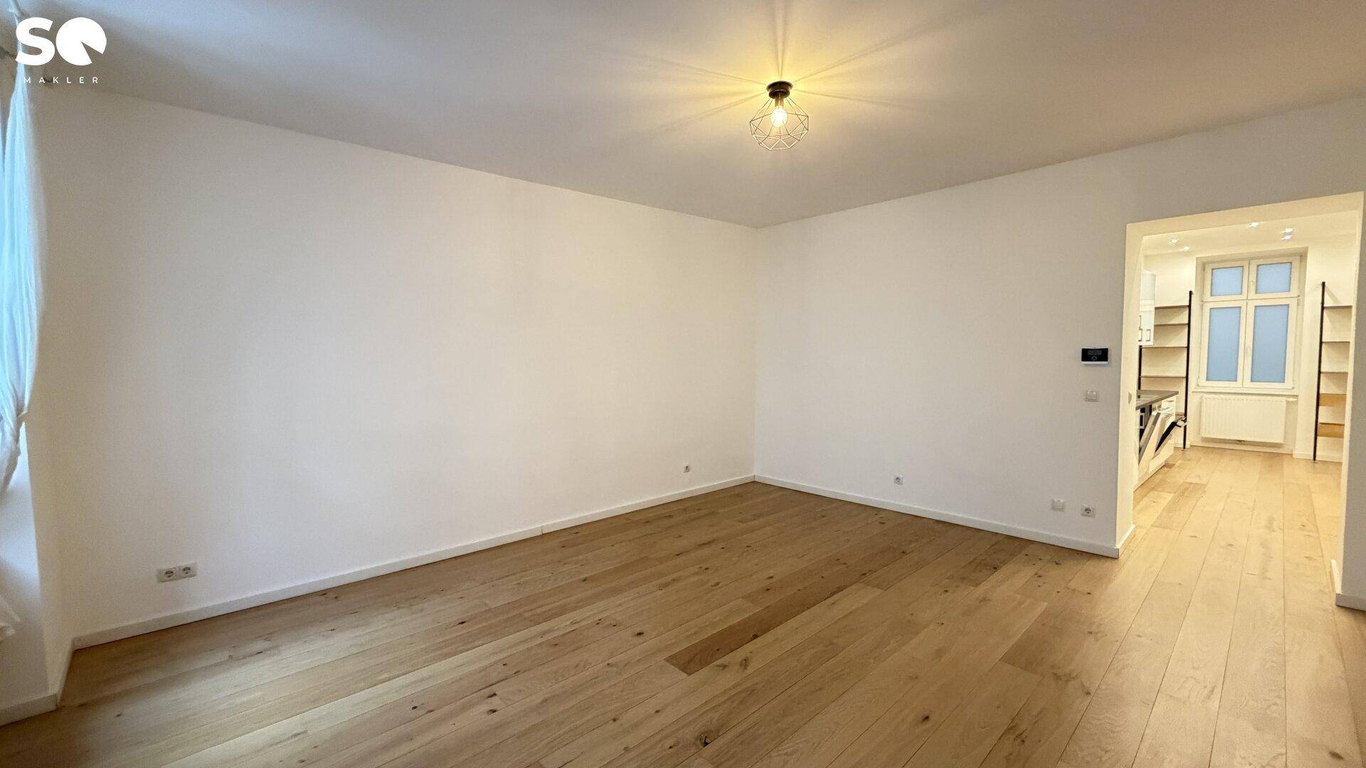 Großes Wohnzimmer mit Parkettboden und Blick in den offenen Küchenbereich, hell und einladend.