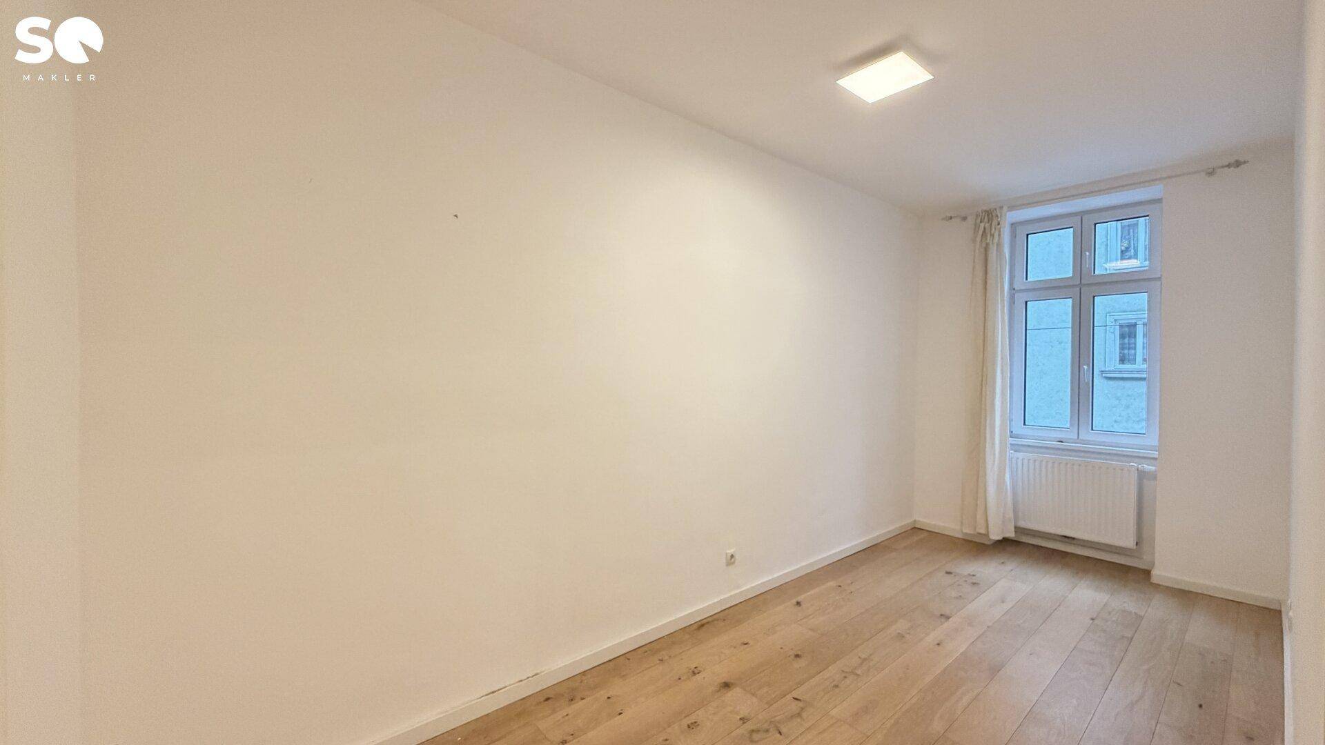 Geräumiges Schlafzimmer mit Parkettboden und einem großen Fenster, das viel Licht hereinlässt.