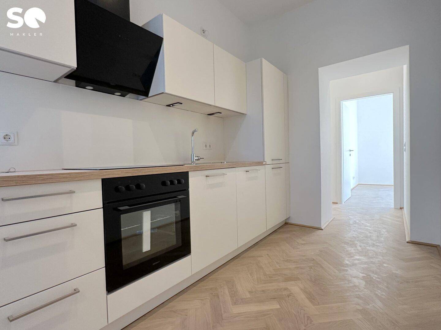 Moderne Einbauküche mit hellen Schränken, Holzarbeitsplatte und integriertem Backofen, daneben Fischgrätparkett.