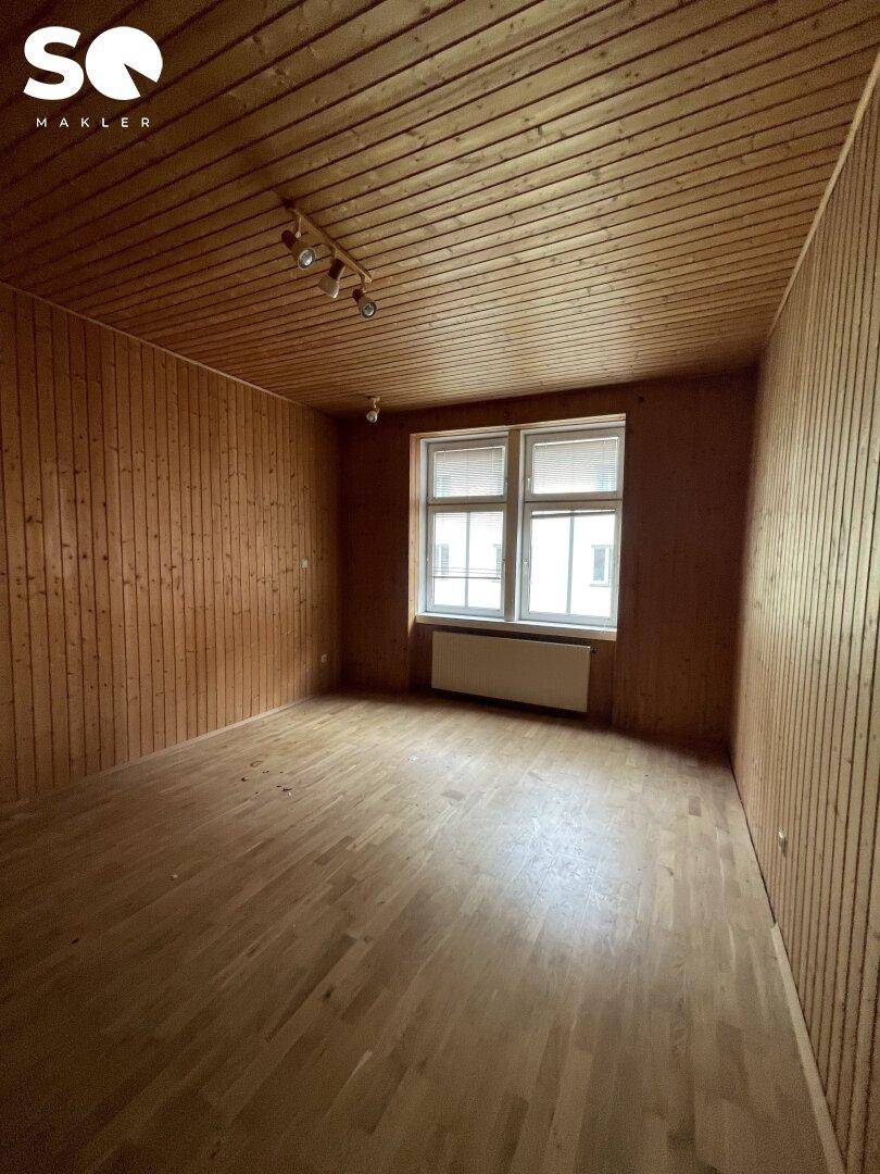 Holzvertäfeltes Zimmer mit Parkettboden und einem Fenster, das Tageslicht hereinlässt.