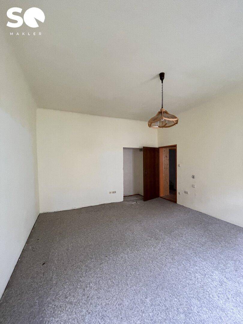 Leeres Zimmer mit Teppichboden und einer Türöffnung, die in einen weiteren Raum führt.
