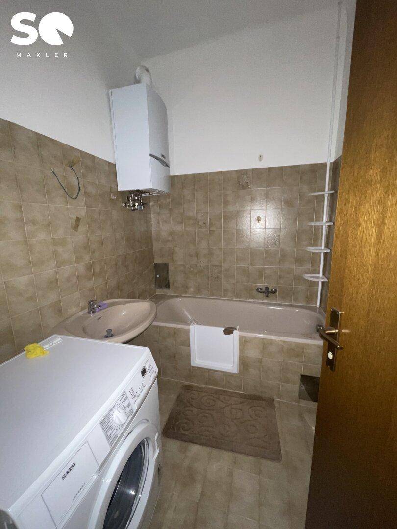 Badezimmer mit Badewanne, Waschbecken und Waschmaschine, in renovierungsbedürftigem Zustand.