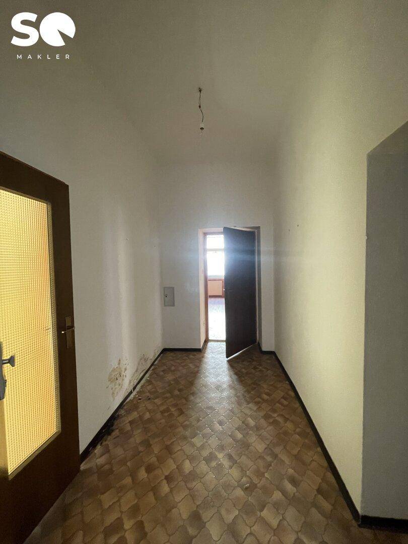 Flur mit gemusterten Fliesen und einer offenen Tür, die Licht in den Raum lässt.