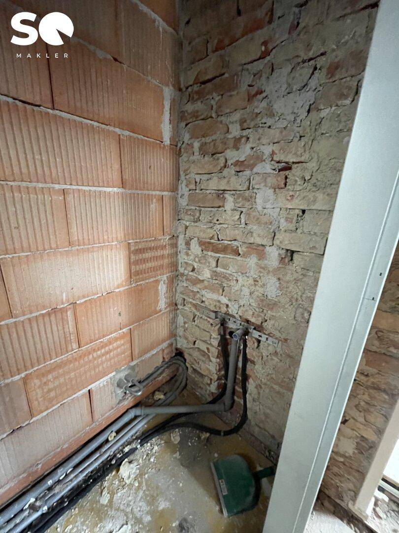 Detailansicht einer Ecke mit freigelegten Ziegelwänden und sichtbaren Installationsrohren.