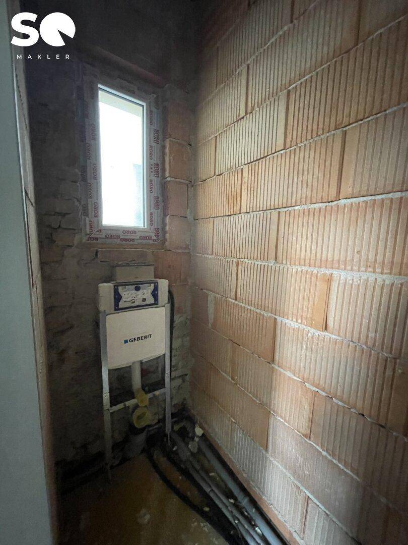 Kleiner Raum im Rohbau mit installiertem WC-Spülkasten und Ziegelwänden.