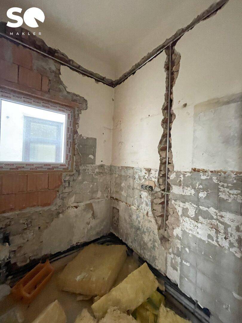 Ecke eines Raumes im Rohbau mit freigelegten Ziegeln und einem kleinen Fenster.