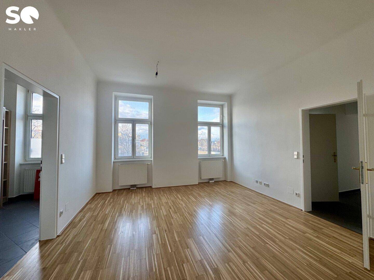 Heller Wohnbereich mit Parkettboden und Zugang zu einem weiteren Raum.