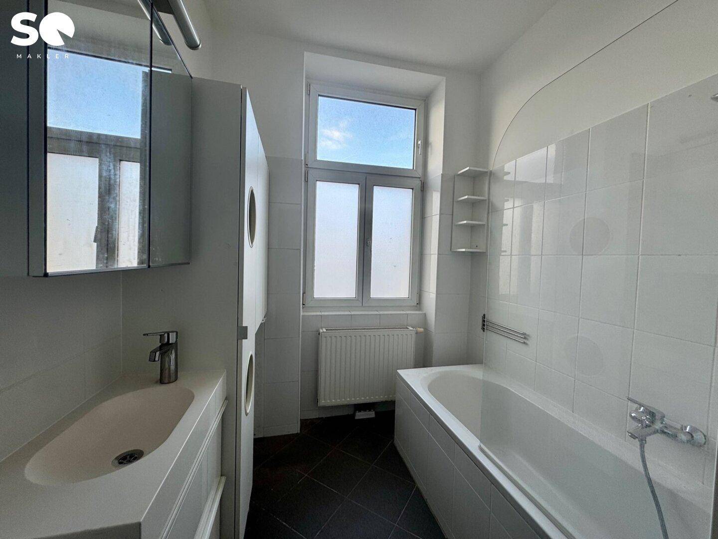 Helles Badezimmer mit Badewanne, Waschbecken und einem Fenster für Tageslicht.