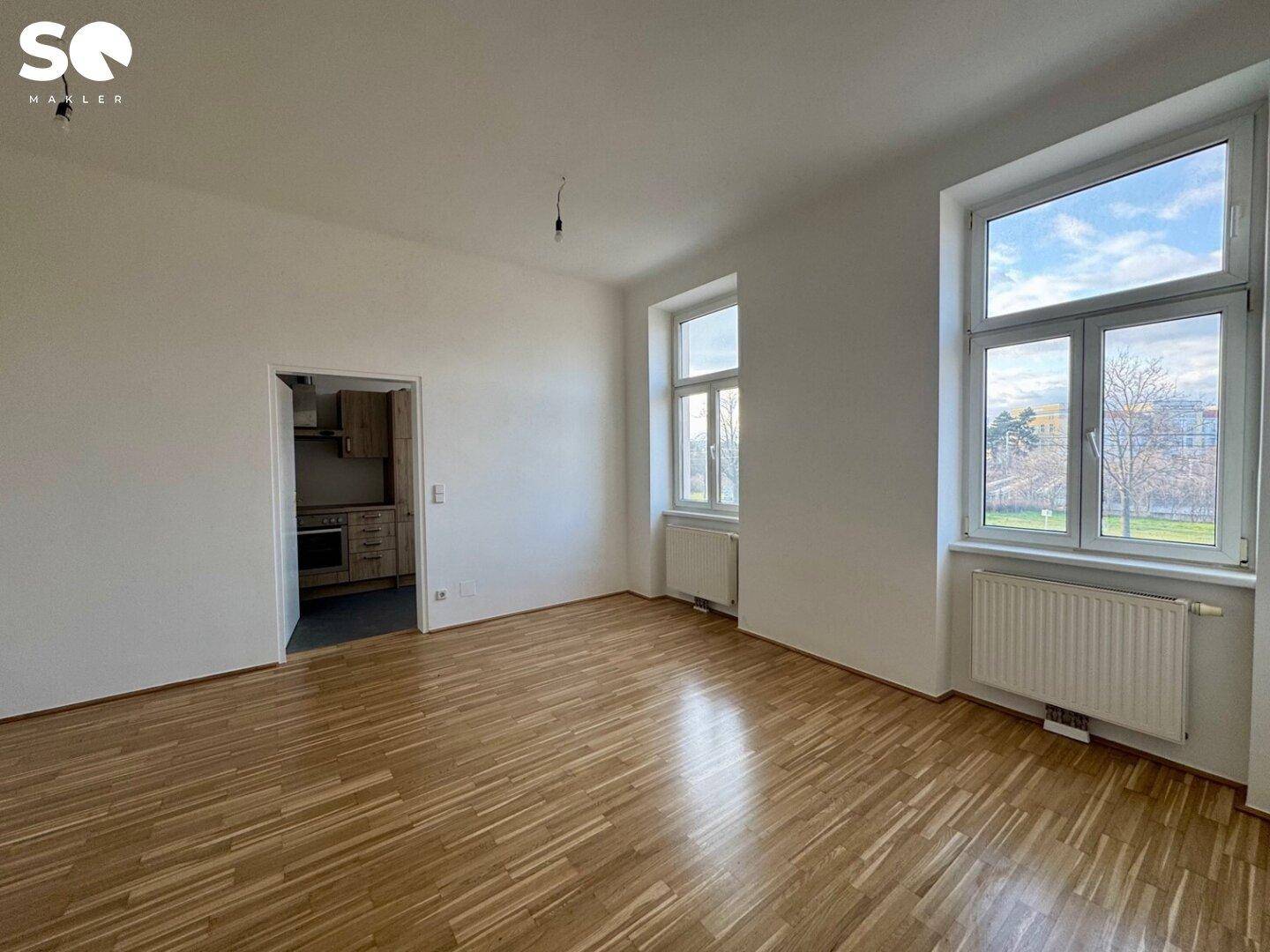 Geräumiges Wohnzimmer mit Parkettboden und Blick ins Grüne durch die großen Fenster.