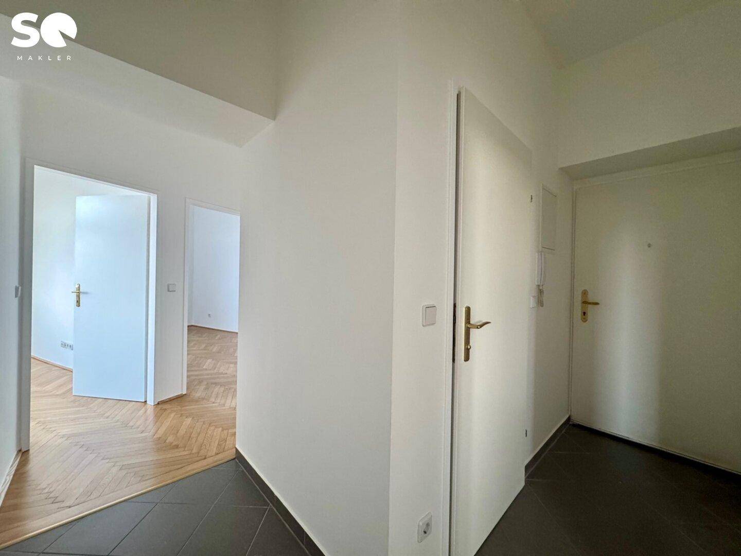 Heller Flur mit dunklen Fliesen und Zugang zu verschiedenen Zimmern der Wohnung.