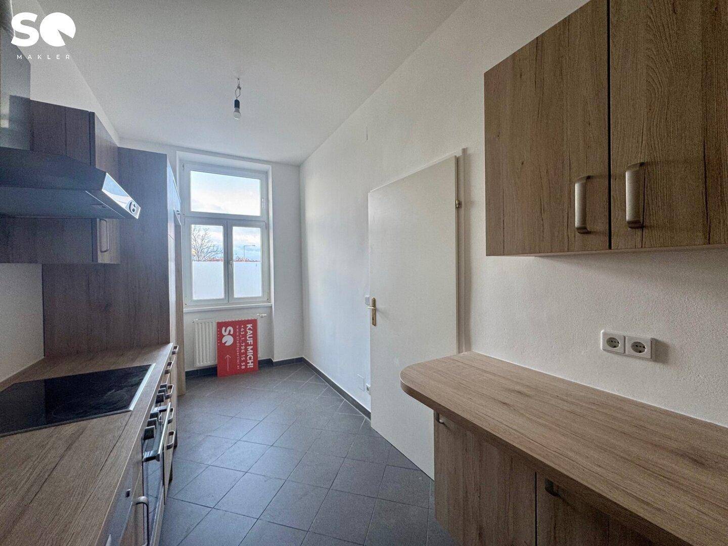 Funktionale Küche mit Holzoptik-Schränken, dunklen Fliesen und einem Fenster.