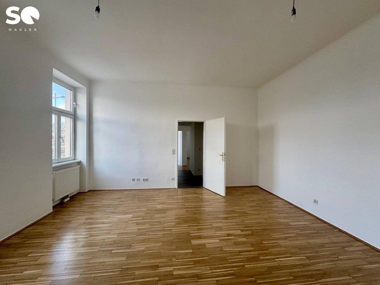 Großzügiges Wohnzimmer mit hellem Parkettboden und viel Tageslicht durch die Fenster.
