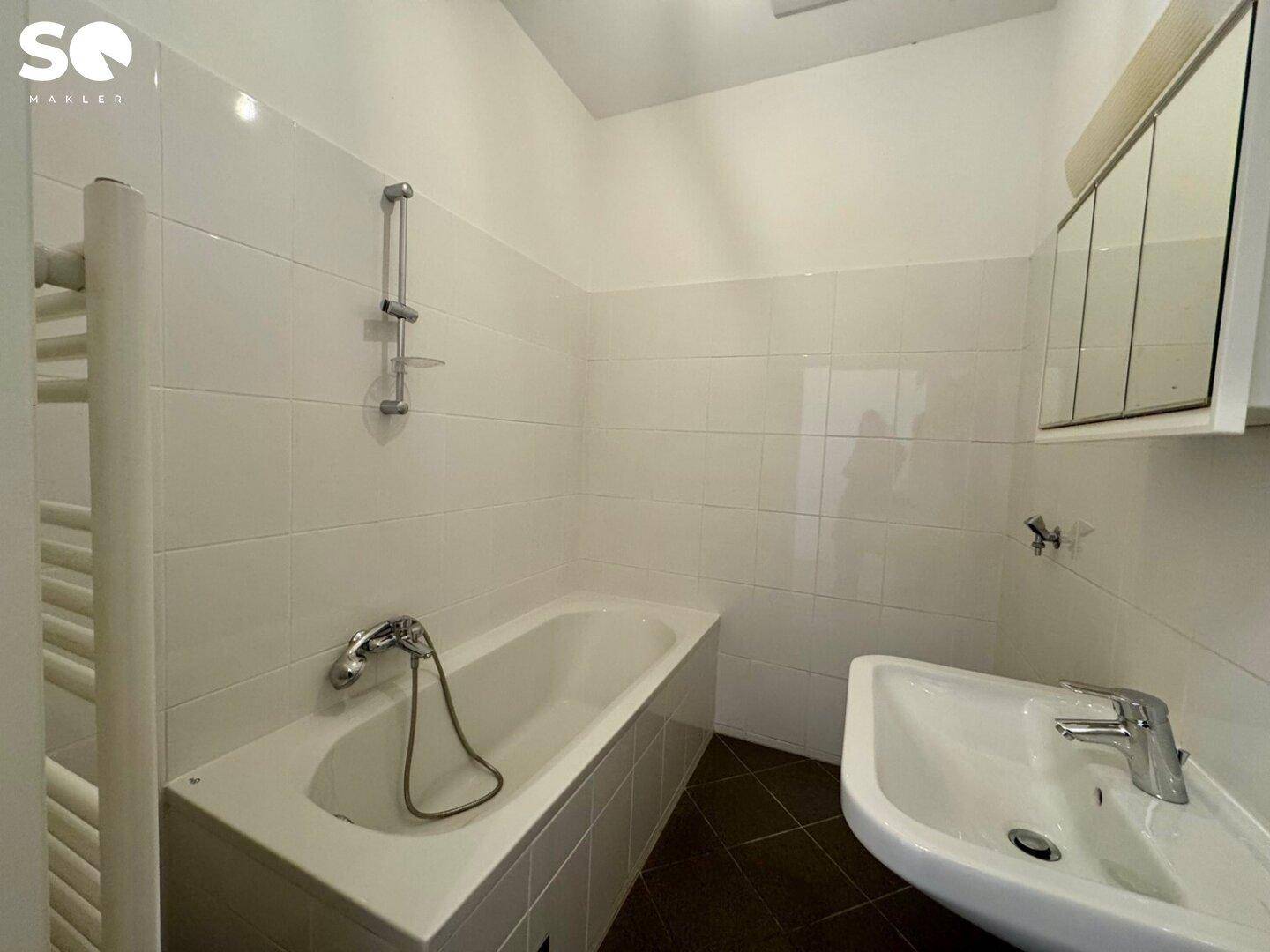 Funktionales Badezimmer mit Badewanne, Waschbecken und weißen Fliesen, ausgestattet mit einem praktischen Spiegelschrank.
