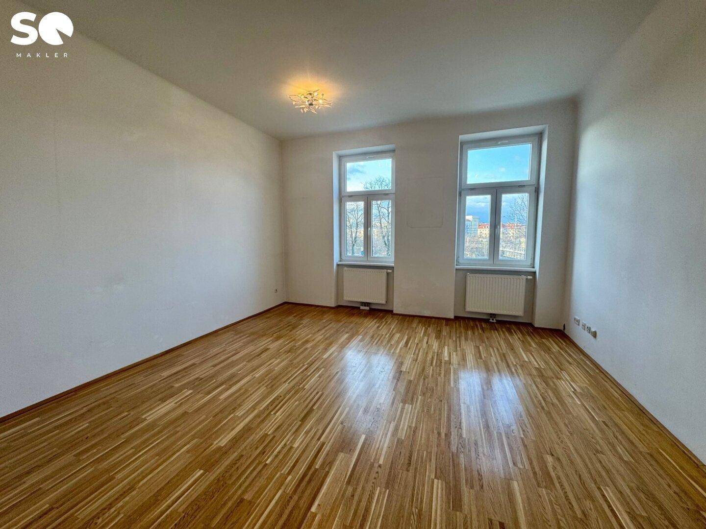 Geräumiges, helles Zimmer mit Parkettboden und zwei großen Fenstern, die eine einladende Atmosphäre schaffen.