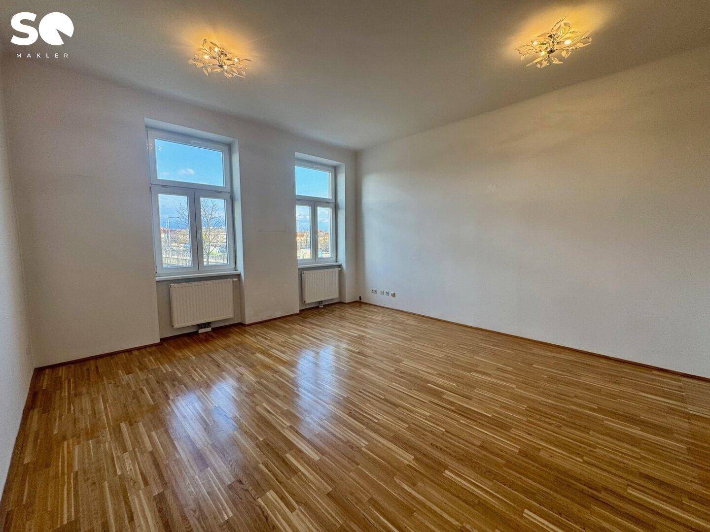 Großes, helles Zimmer mit glänzendem Parkettboden und zwei Fenstern, die den Raum angenehm erhellen.