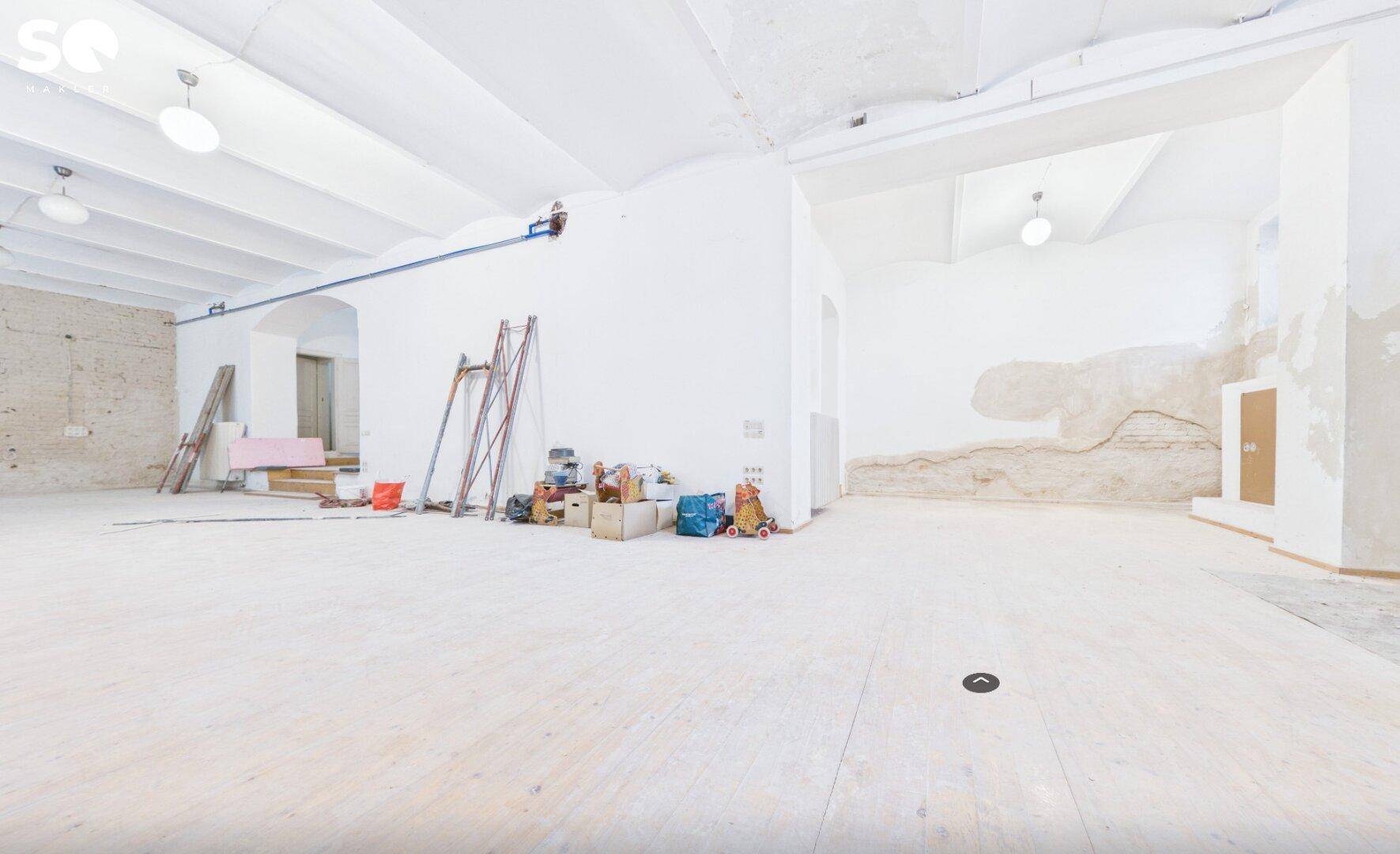 Weiterer Blick in den großen, leeren Raum im Rohbau mit Baustellenausrüstung und hohen Decken.