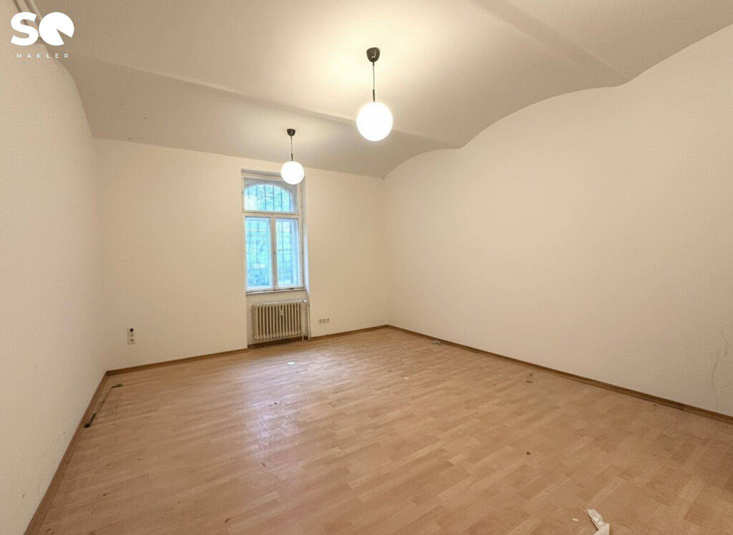 Leerer Raum mit Parkettboden, einem Fenster und zwei Deckenleuchten, bereit zur Renovierung.