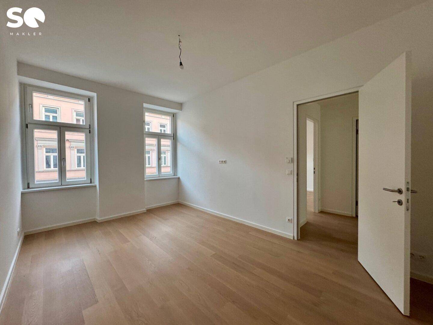 Unmöbliertes Schlafzimmer mit hellem Holzboden und zwei Fenstern mit Blick auf die Nachbarschaft.