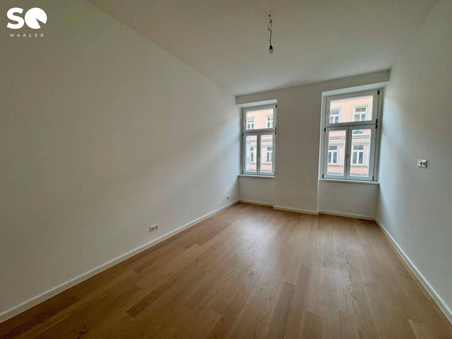 Helles, leeres Zimmer mit Parkettboden und zwei Fenstern, ideal als Schlaf- oder Arbeitszimmer.