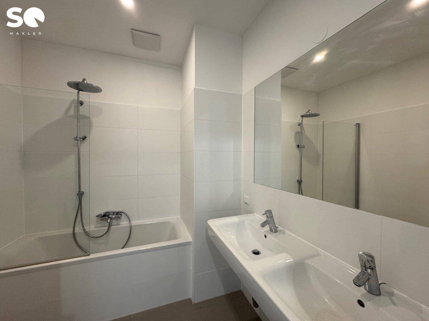 Modernes Badezimmer mit weißen Fliesen, Badewanne mit Duschfunktion und Doppelwaschbecken.