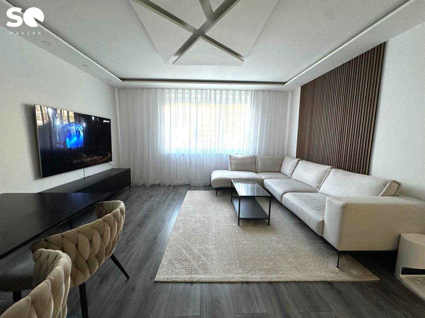 Geräumiger Wohnbereich mit beigem Ecksofa, Couchtisch und dekorativer Wandverkleidung.