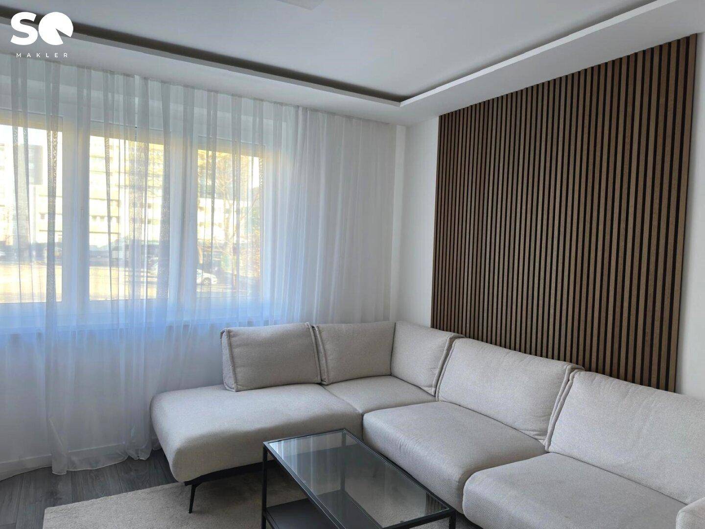 Gemütlicher Wohnbereich mit großem Ecksofa, transparenten Vorhängen und Holzwand.
