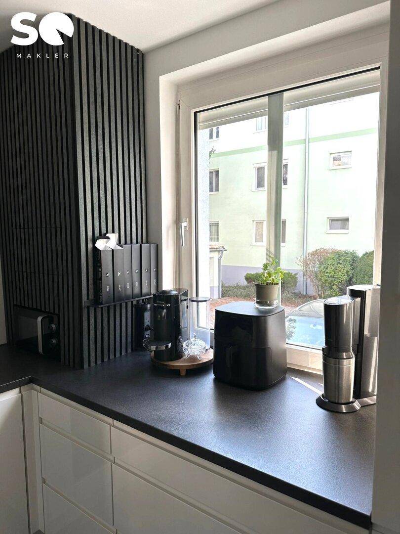 Detailansicht der modernen Küche mit dunkler Arbeitsplatte und Fensterblick ins Grüne.