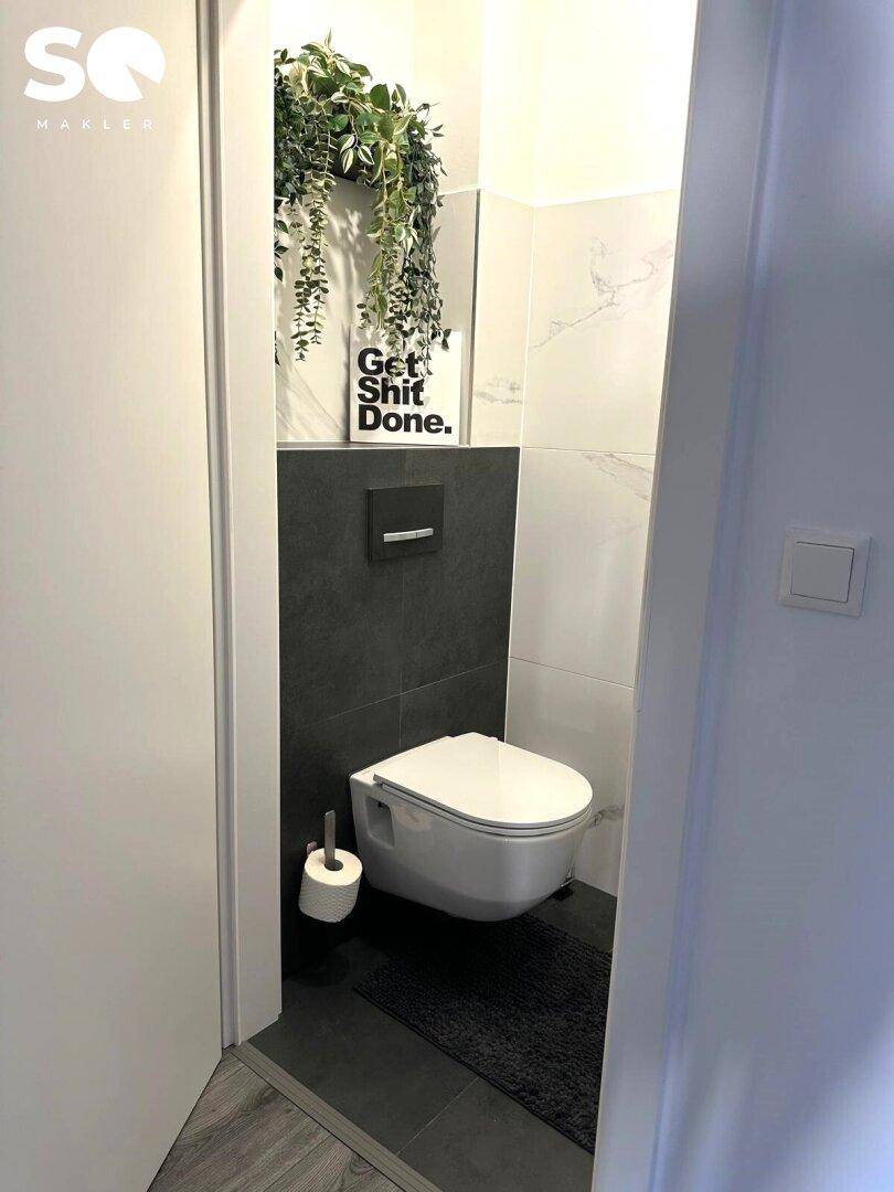 Kompaktes Gäste-WC mit wandhängender Toilette und moderner Fliesenverkleidung.