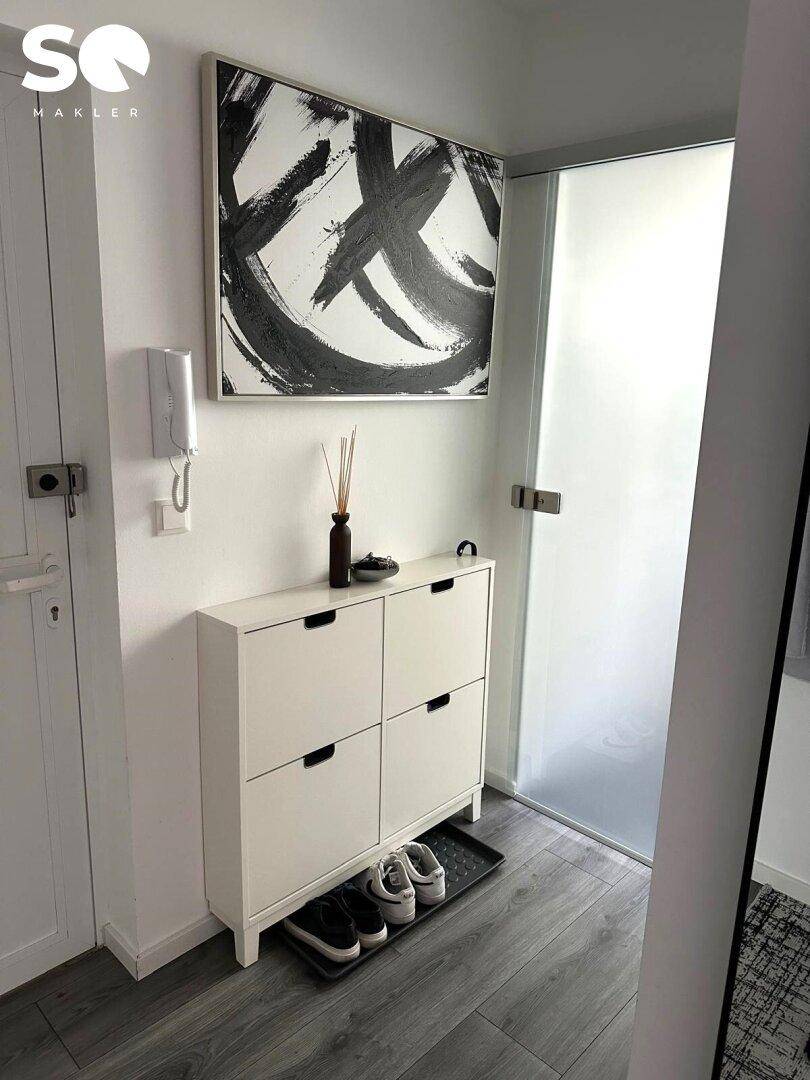 Eingangsbereich mit Schuhschrank, moderner Kunst und Milchglastür für Privatsphäre.