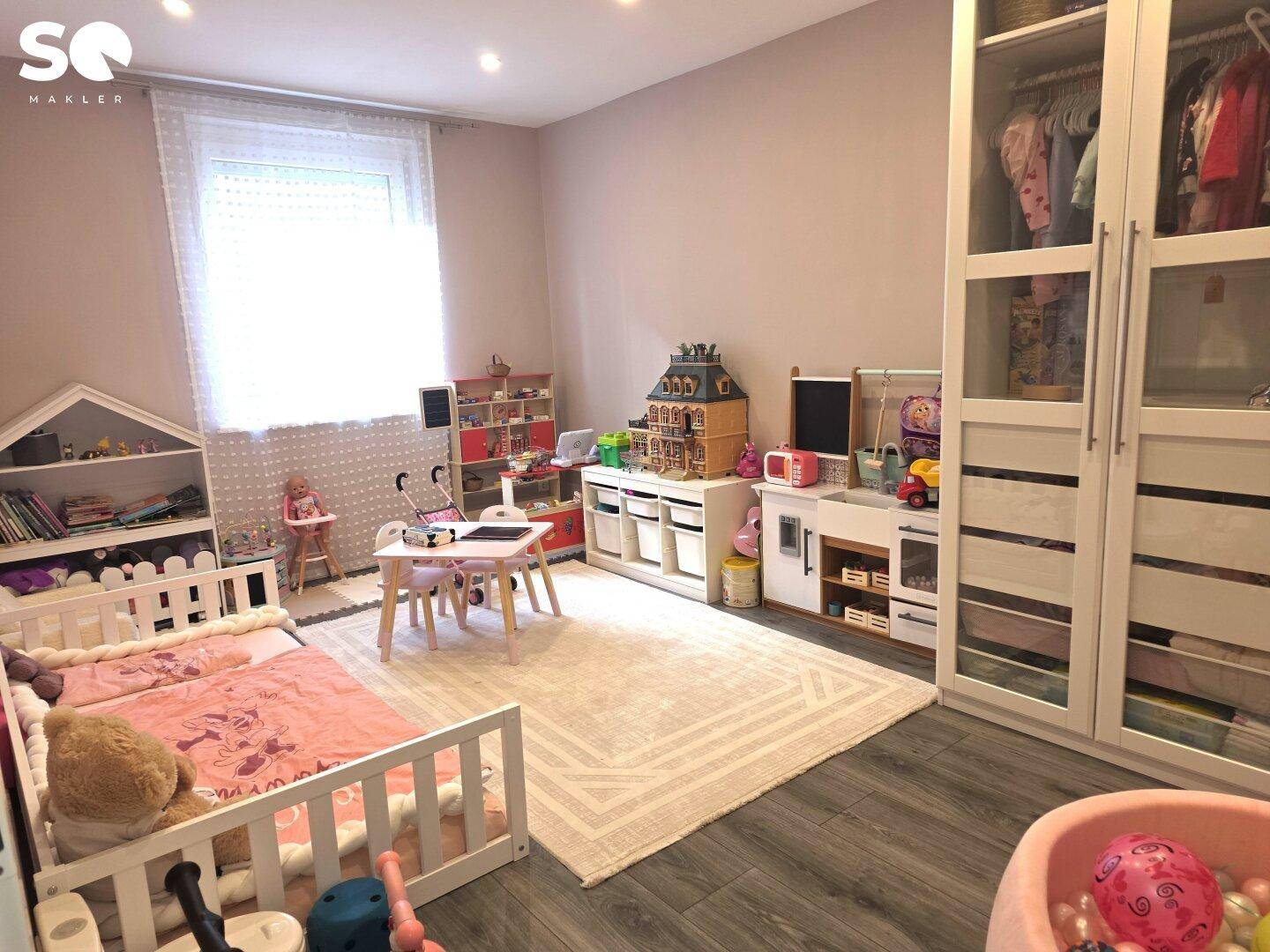 Helles Kinderzimmer mit Spielzeug, weißem Bett und großem Kleiderschrank.