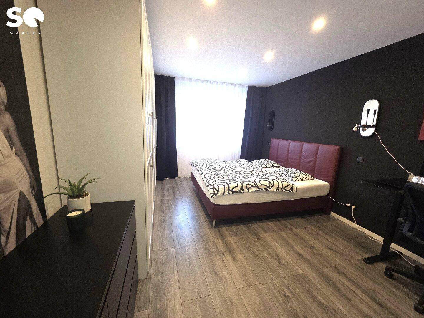 Modernes Schlafzimmer mit dunklen Wänden, rotem Bett und Holzboden.