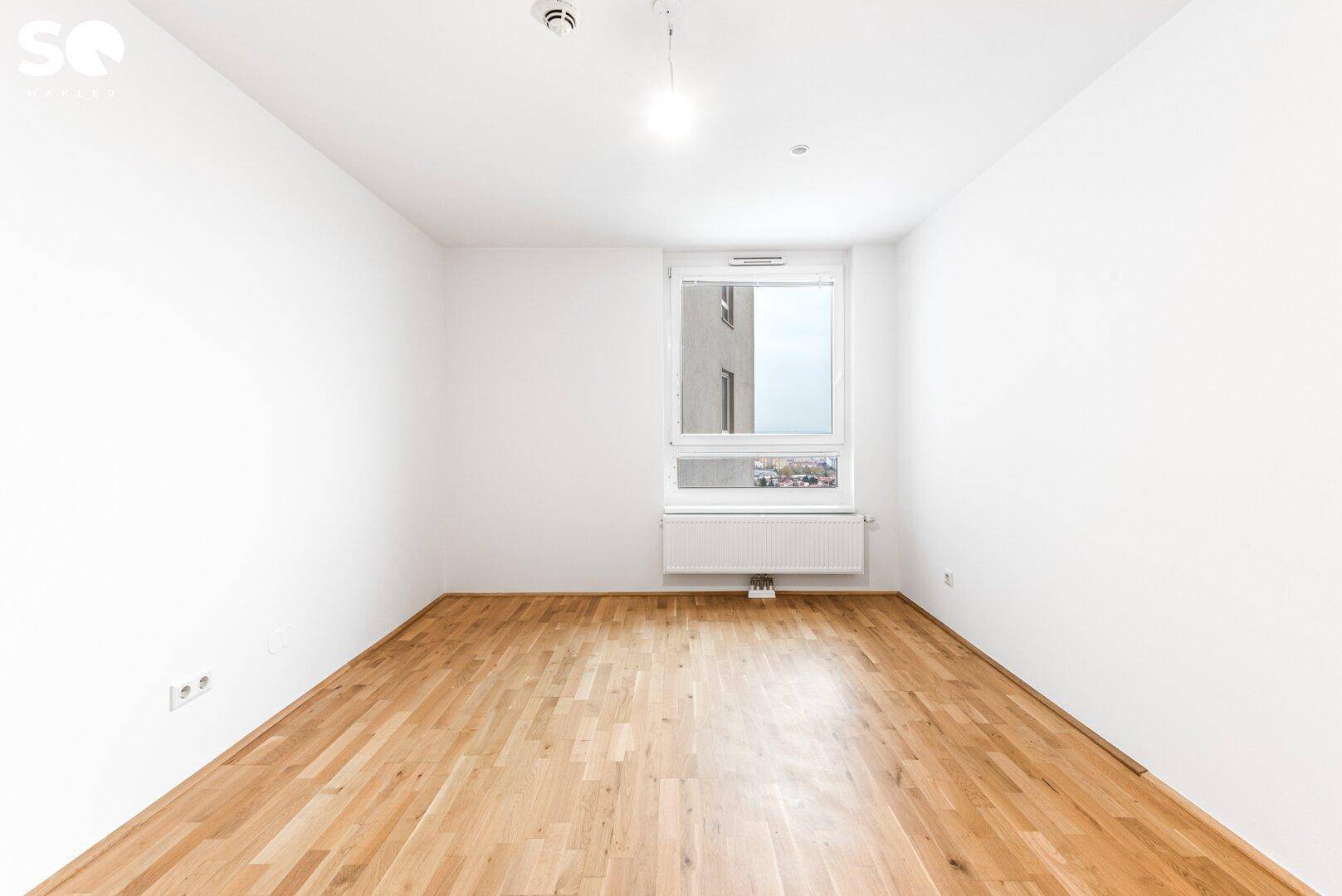 Leeres Schlafzimmer mit Parkettboden und einem großen Fenster für viel Tageslicht.