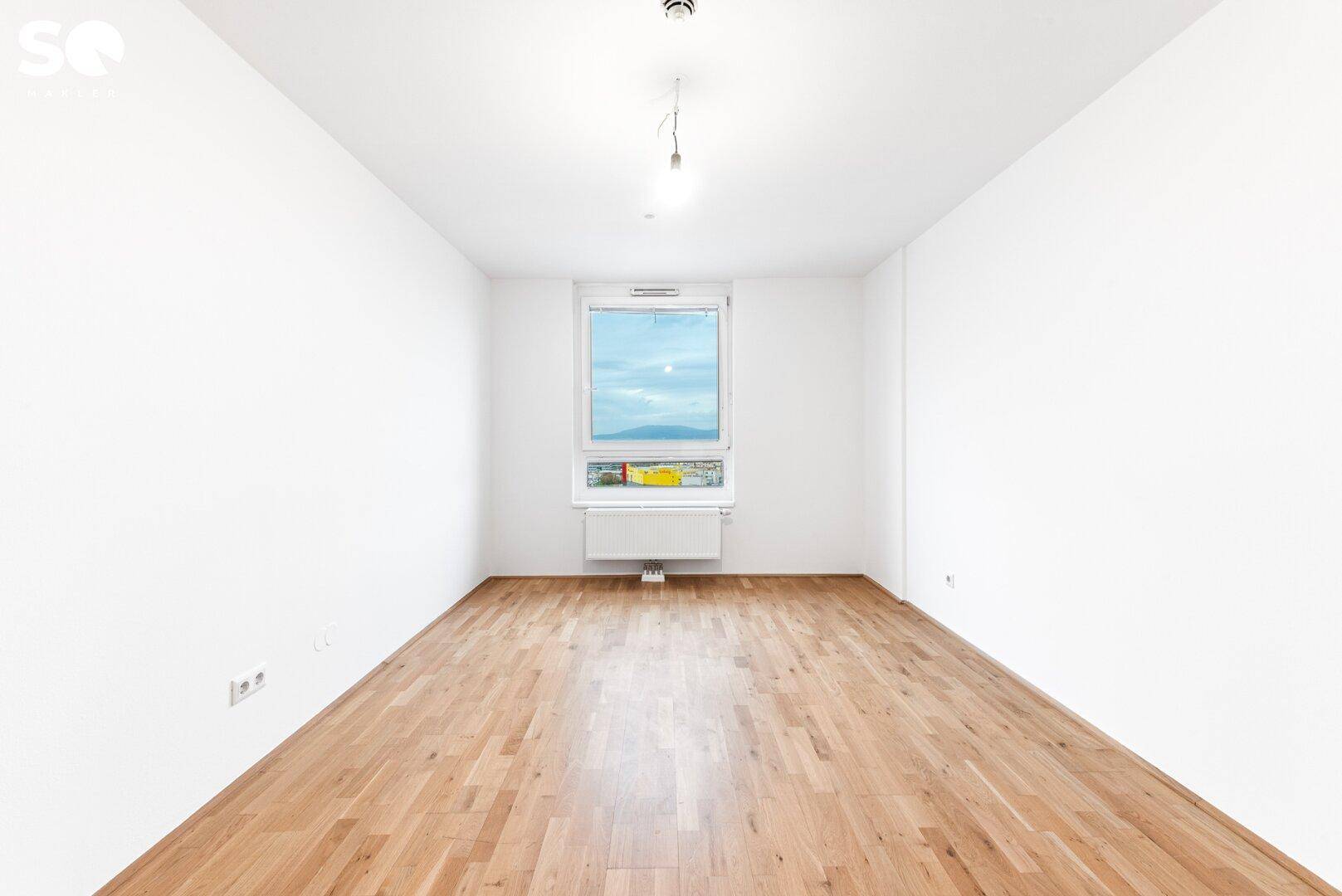 Helles Schlafzimmer mit Parkettboden und einem großen Fenster für viel Tageslicht.