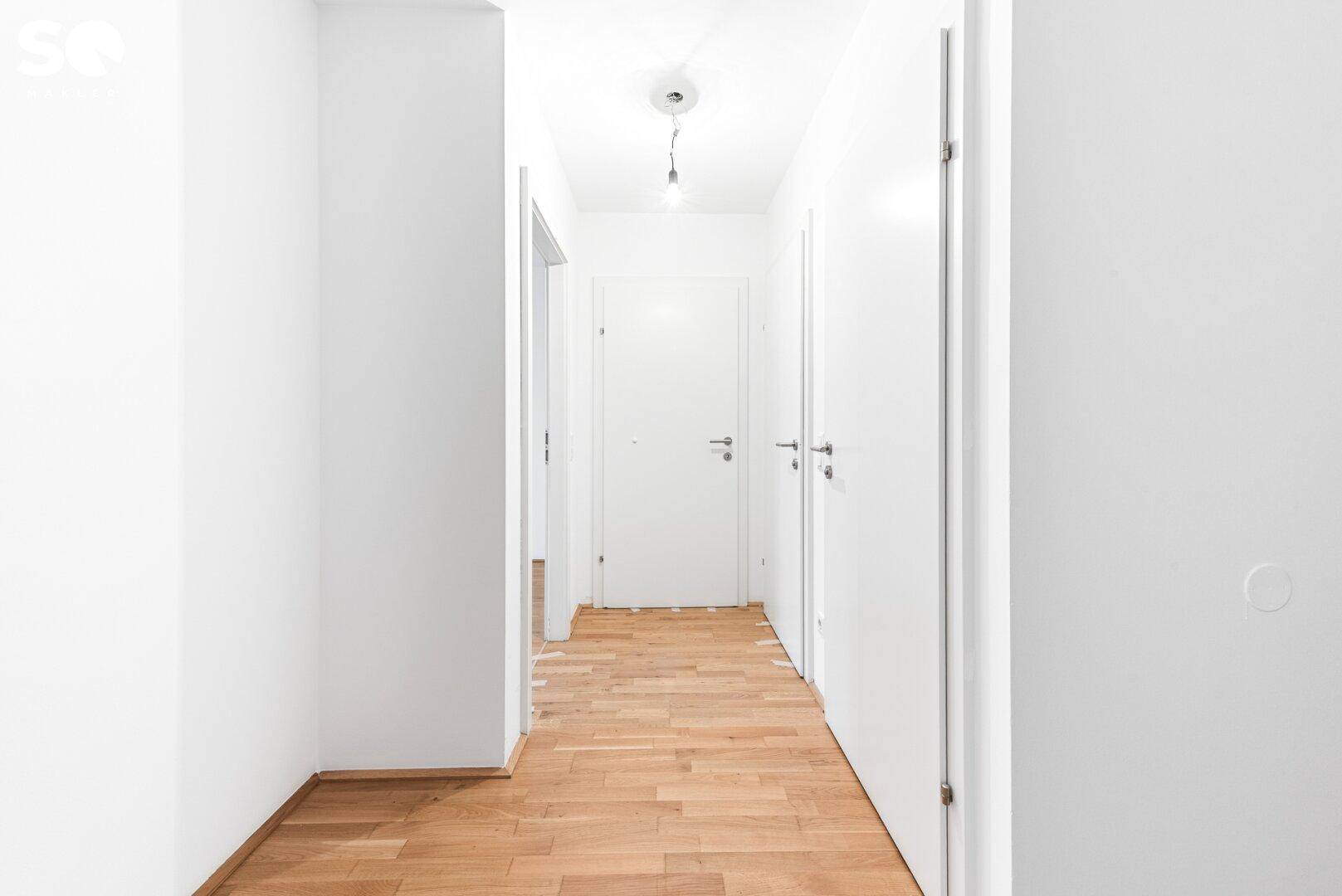 Heller Flur mit Holzboden und mehreren weißen Türen, der verschiedene Räume verbindet.
