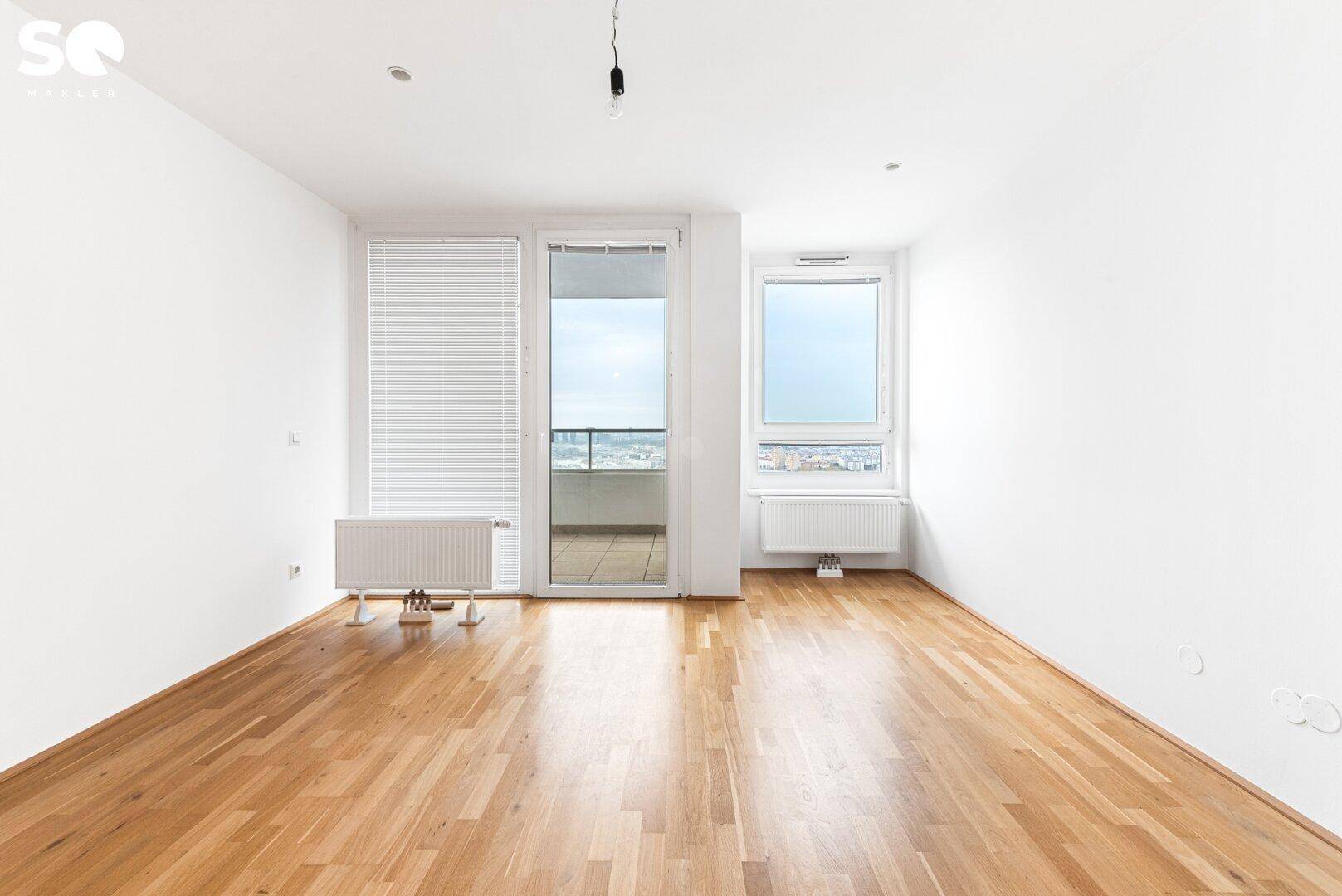 Geräumiges Wohnzimmer mit großen Fenstern, viel Tageslicht und Zugang zum Balkon.