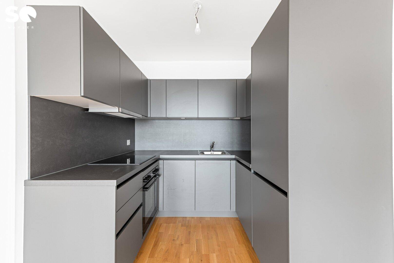 Moderne Küchenzeile in Grau mit integrierten Geräten und dunkler Arbeitsplatte.