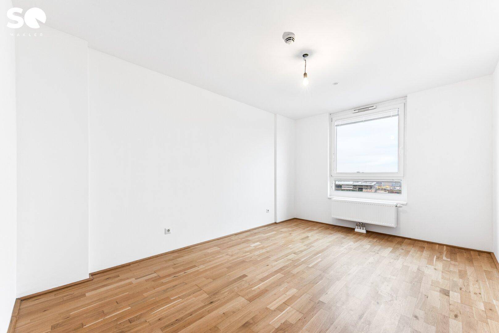 Helles Schlafzimmer mit Parkettboden, weißen Wänden und einem großen Fenster.