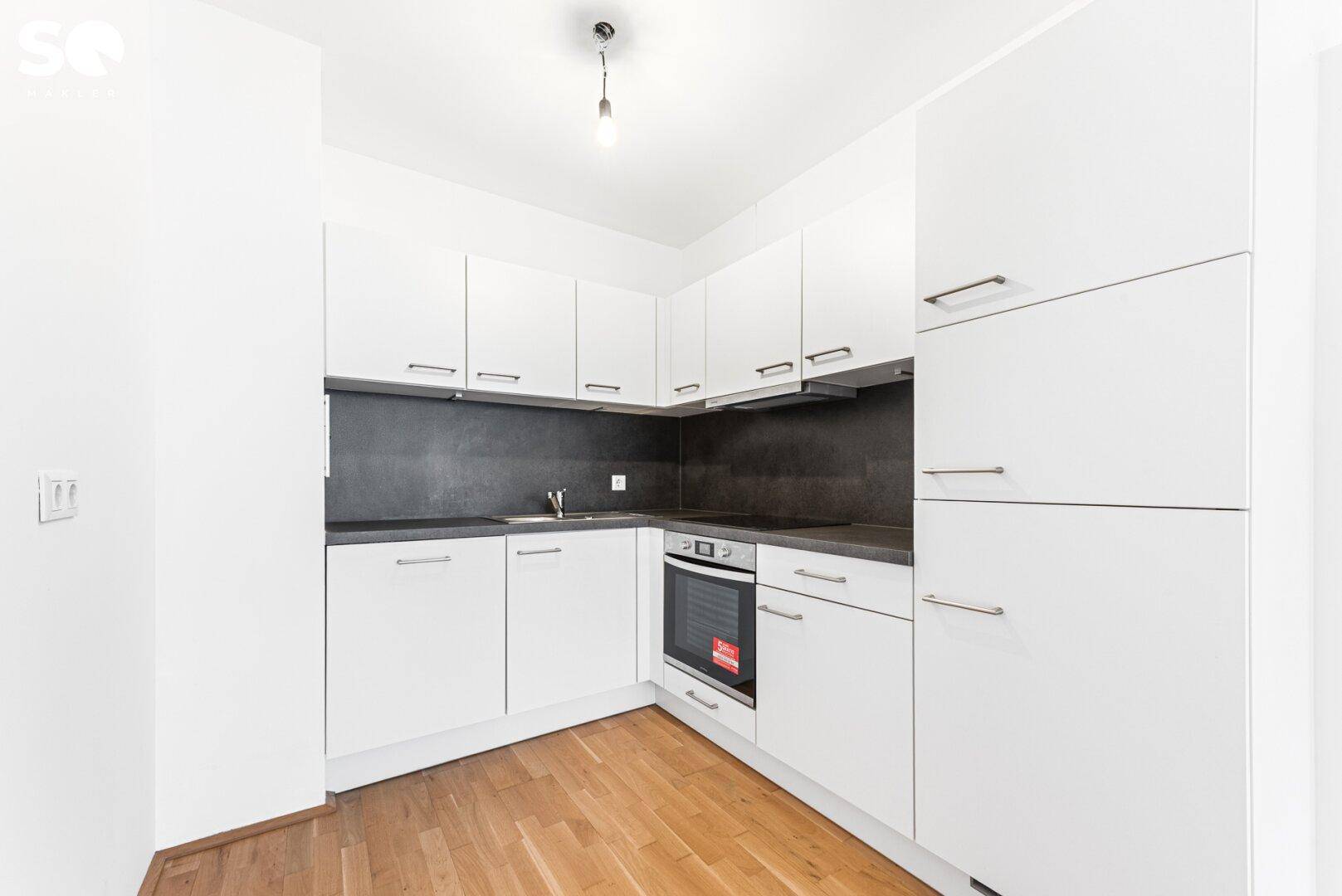 Moderne Einbauküche mit weißen Schränken, dunkler Arbeitsplatte und integriertem Backofen.