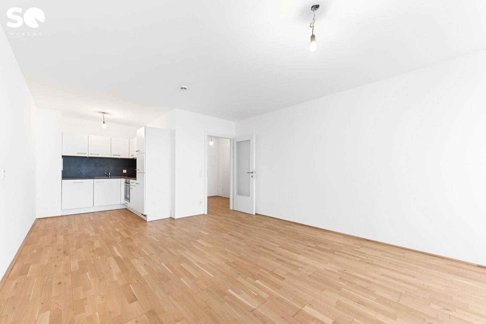 Offener Wohnbereich mit Parkettboden und integrierter Küchenzeile in modernem Design.