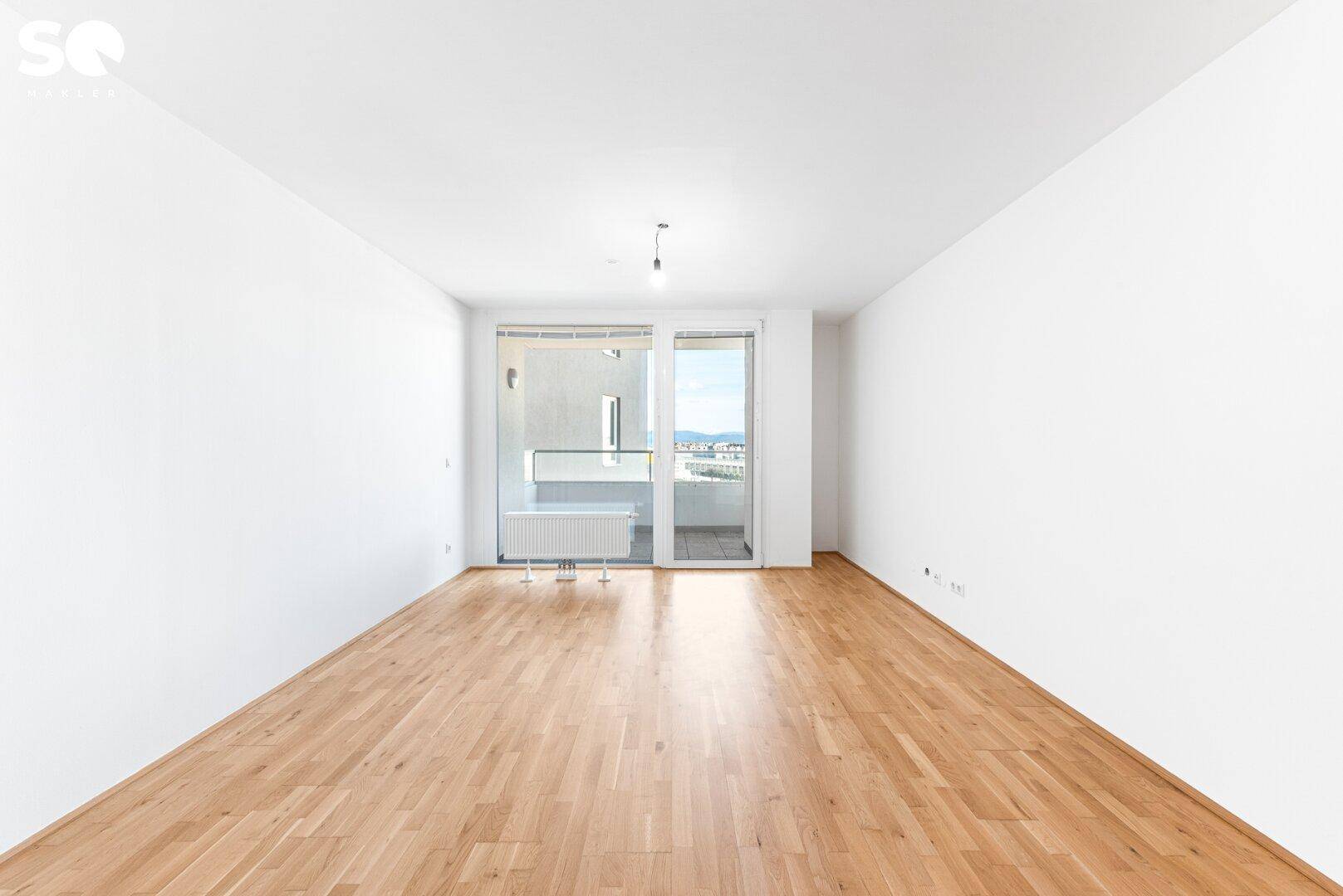Leeres, helles Wohnzimmer mit Parkettboden und Zugang zu einem Balkon mit Stadtblick.