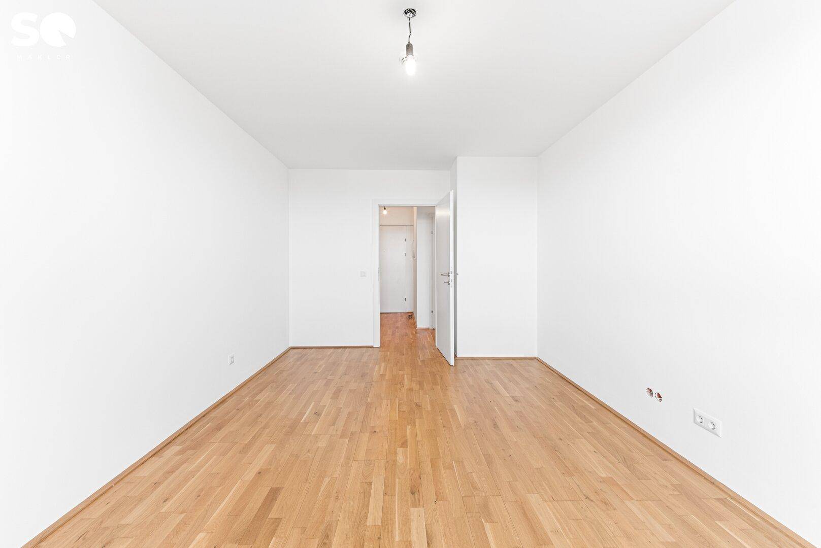 Helles, leeres Zimmer mit Parkettboden und Zugang zu einem weiteren Bereich der Wohnung.